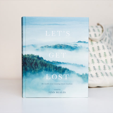 A large hard back book called 'Let's Get Lost'. The whimsical cover shows soft white clouds with tree topped hills poking through the top of the clouds.