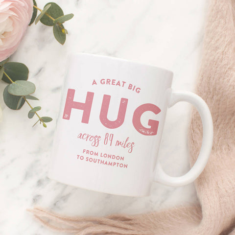 A white ceramic mug with pink text reading "A great big hug across 89 miles, from London to Southampton.