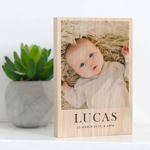 A personalised new baby wooden photo block. A photo of a baby is printed on to a solid block of oak, underneath the photo are the words 'Lucas, 20 March 2018. 8.46PM'.