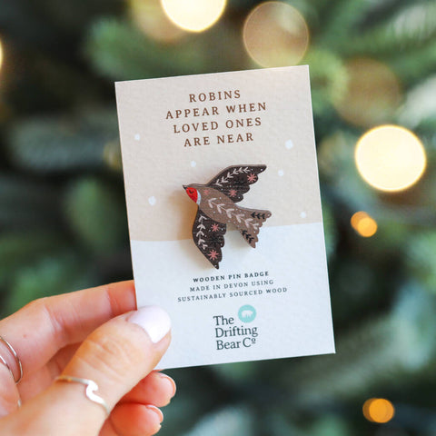 A decorative robin pin badge, made from sustainable wood on a card that reads "ROBINS APPEAR WHEN LOVED ONES ARE NEAR". 